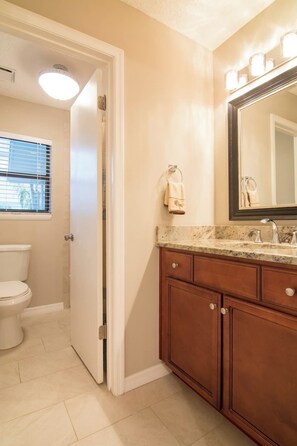 A bathroom with a toilet, a sink with a mirror, and a towel hanging on the wall. - Pure Relaxation: heated pool, beach, cabana & more (St. Augustine)