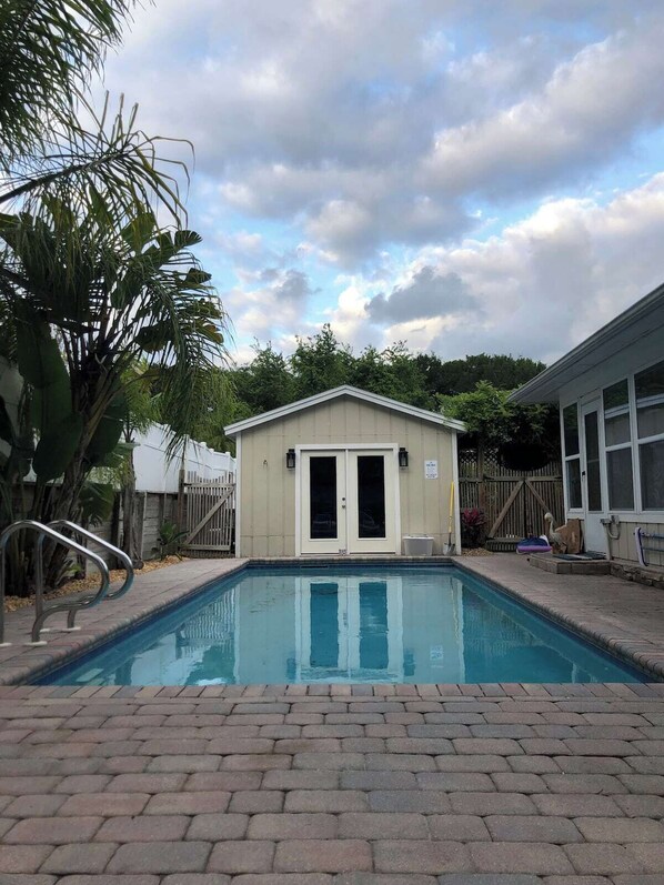 A swimming pool with a brick border, a small shed with a door, and a metal handrail. - Pure Relaxation: heated pool, beach, cabana & more (St. Augustine)