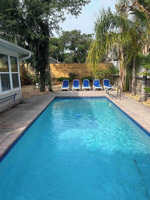 A rectangular swimming pool with clear blue water, surrounded by a brick deck. There are five blue lounge chairs aligned along the pool's edge. - Pure Relaxation: heated pool, beach, cabana & more (St. Augustine)