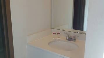 Un baño con un lavabo blanco, un espejo y dos botellas de jabón.