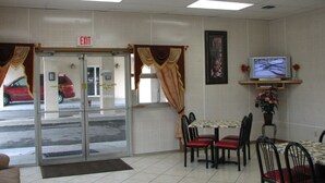 A restaurant with an exit sign, a dining area with chairs and a table, and a television on the wall. - The Hastings Inn Parsons  (Parsons)