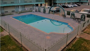 A swimming pool with a fenced area, a covered car parking section, and a building with multiple balconies. - The Hastings Inn Parsons  (Parsons)