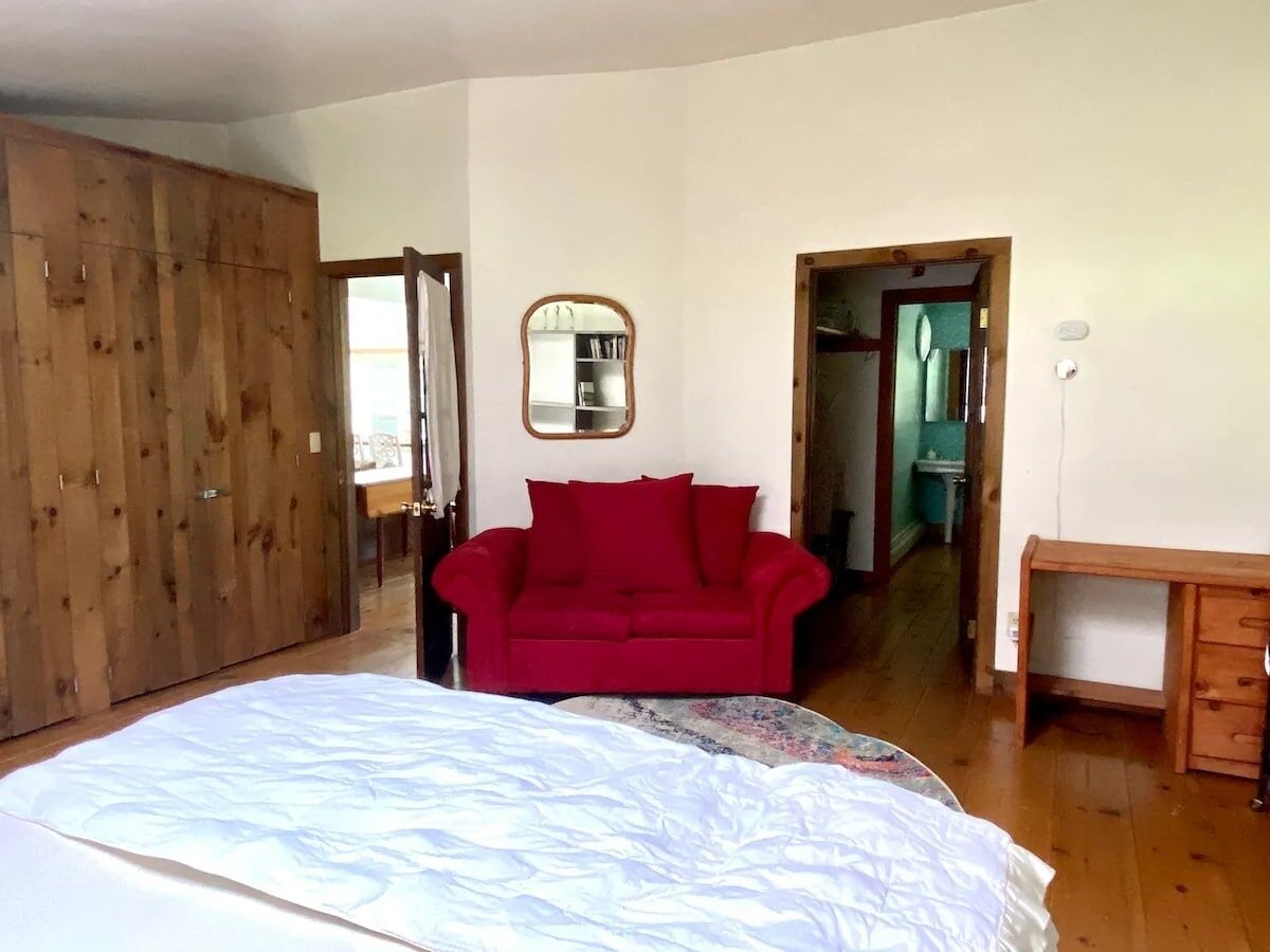 Ein Schlafzimmer mit einem großen Bett, einem roten Sofa, einem Holzschrank und einem Schreibtisch.