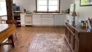 A kitchen with white cabinets, a wooden dining table, and a large window. - 1800s Carriage house in Berkshires / Hudson Valley (New Lebanon)