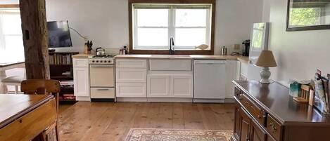 A kitchen with white cabinets, a wooden dining table, and a large window.