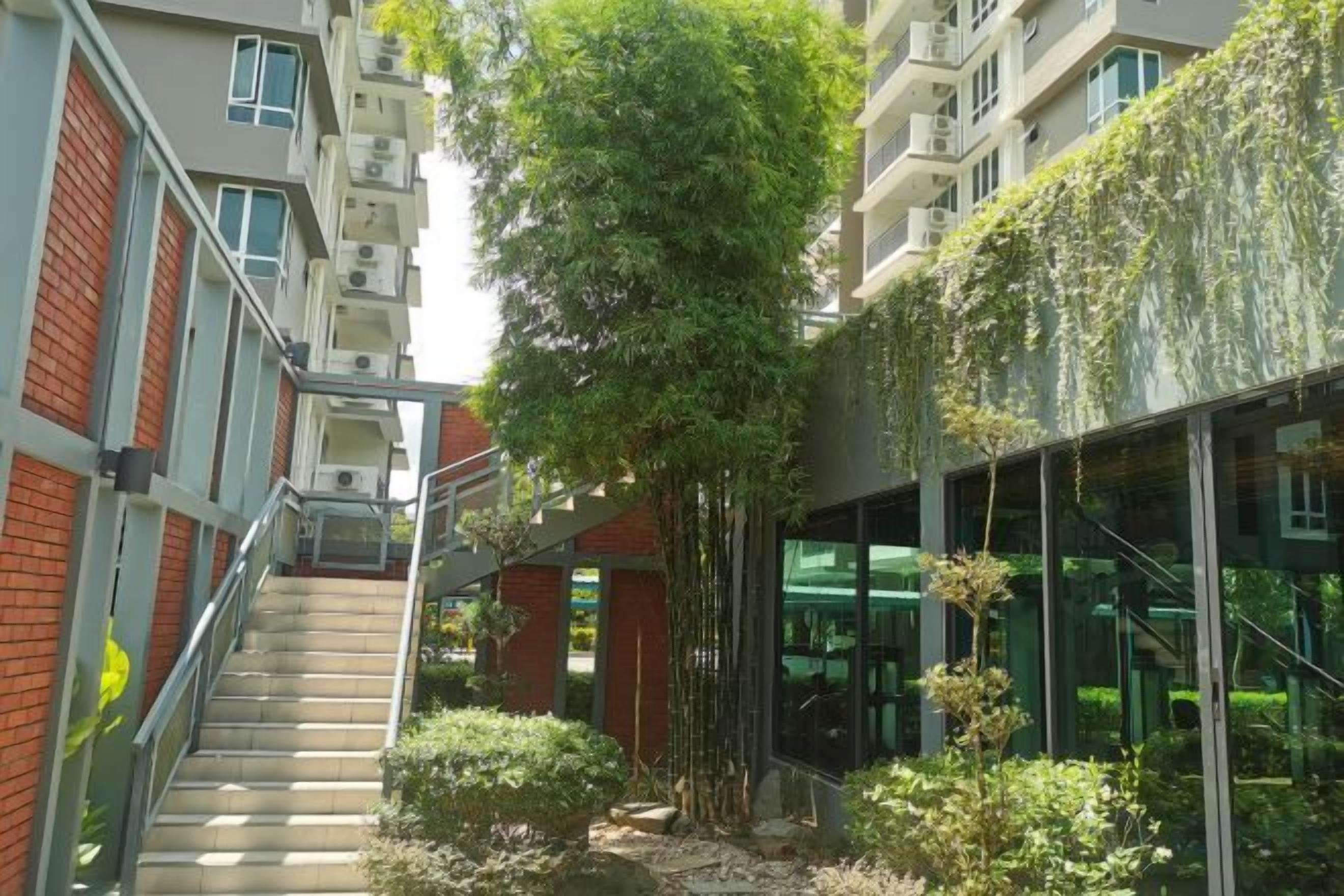 A multi-story building with a central staircase, glass facade, and greenery.
