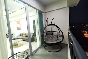 A balcony with a hanging chair, a sliding glass door leading to a living area, and a city view at night. - Homexuite Vacation Condo Sri Indah (Sandakan)