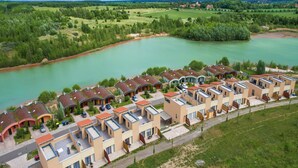 A modern hotel with multiple-story buildings, a parking area, and a river in the background. - Luxuriose Ferienwohnung am Stormthaler See (Grossposna)