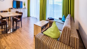 A modern living room with a dining area, green curtains, a sofa, and a TV. - Luxuriose Ferienwohnung am Stormthaler See (Grossposna)