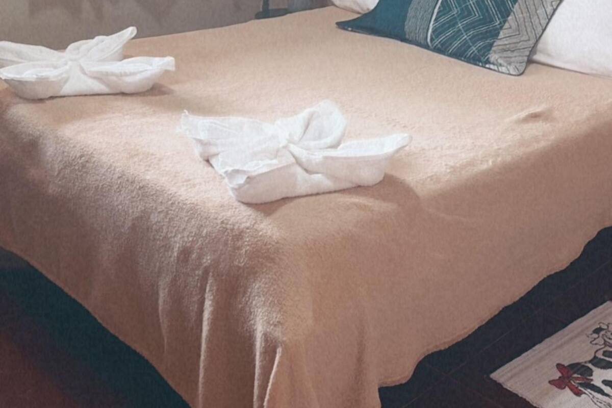 A neatly made bed with a beige bedspread and two pillows, one with a geometric pattern.