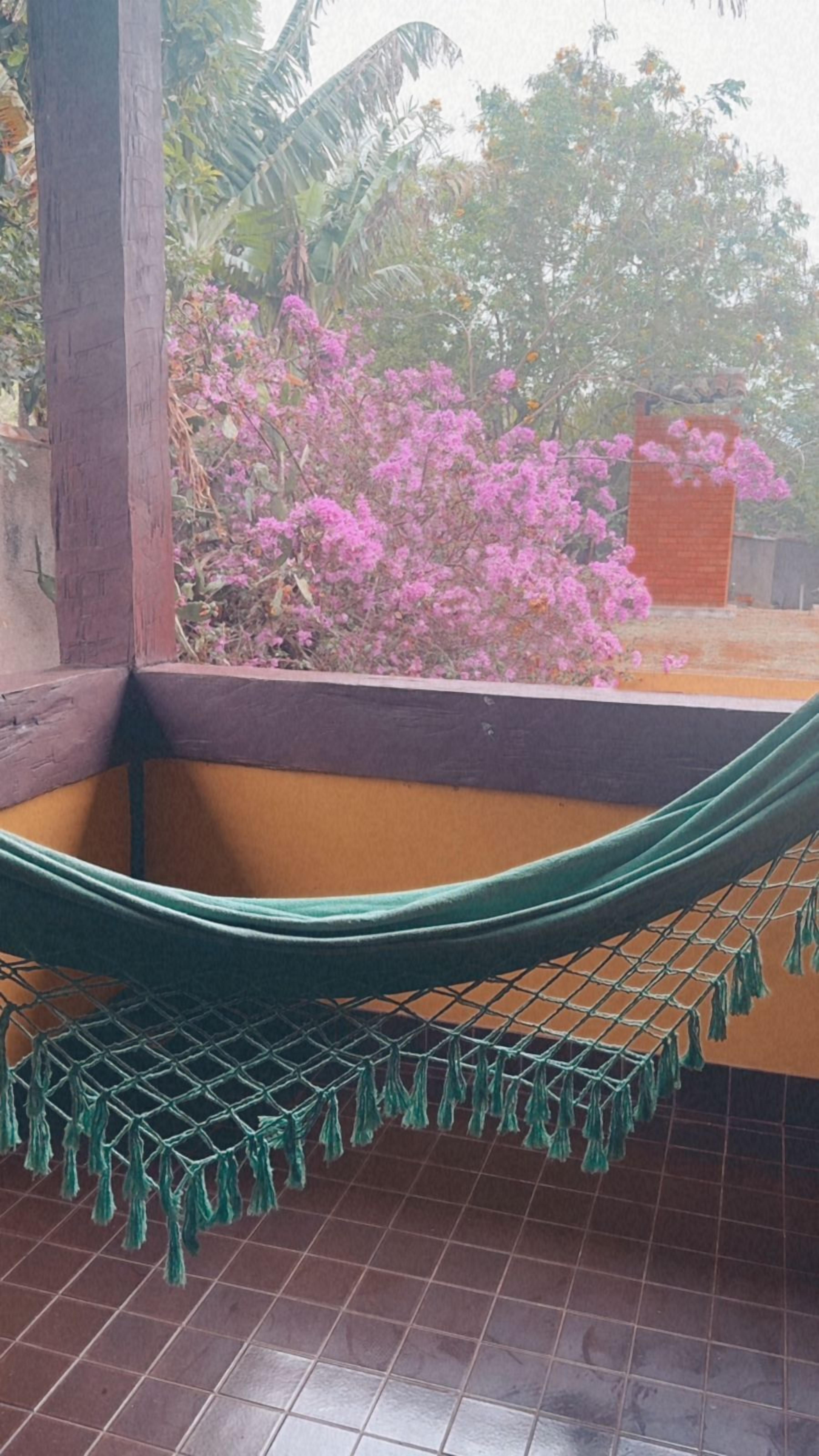 Un hamac installé dans un coin, offrant une vue sur des fleurs roses et un mur de briques.