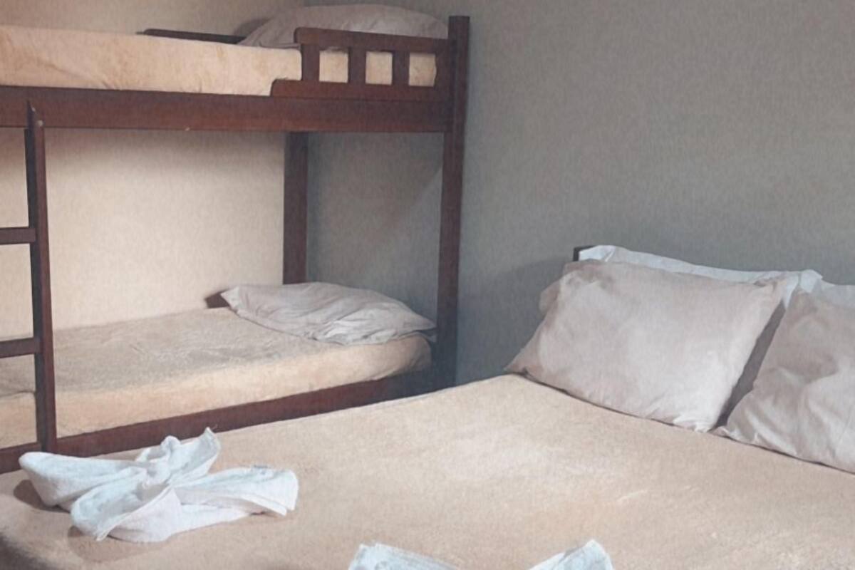 A single bed with a neatly folded towel and a bunk bed above it in a room with plain walls and a visible air conditioning unit.