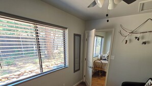 Une pièce dotée d’un ventilateur de plafond, d’une fenêtre avec des stores, d’une porte donnant sur une autre pièce et d’un tapis à motifs.