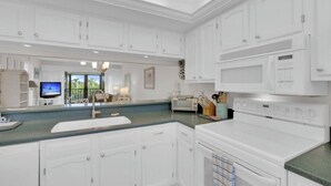 A modern kitchen with white cabinetry, a large island, a built-in microwave, and a view to the living area. - Charming 2b-2b condo in beautiful Fort Myers Beach- 10 min walk to the beach .  (Fort Myers Beach)