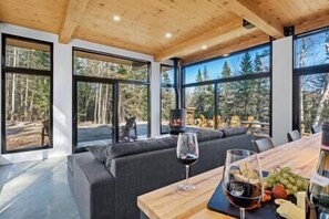 Un interior moderno con un ventanal grande, una chimenea y una zona de estar con una mesa lista para comer.