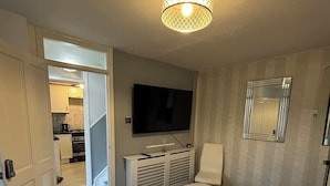 A bedroom with a large bed, a television mounted on the wall, a mirror, and a hallway leading to a kitchen. - K Sweets Bromley Apartments (Bromley)