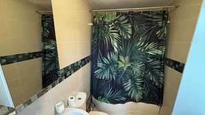 A bathroom with a bathtub, toilet, sink, and a shower curtain with a tropical leaf pattern. - K Sweets Bromley Apartments (Bromley)