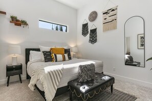 Un dormitorio con cama, mesitas de noche, ventana, decoración en la pared y espejo.
