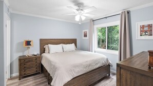 Un dormitori amb un llit de fusta, una nitzeta, un ventilador de sostre i una finestra amb cortines.