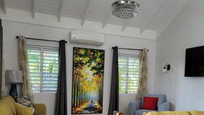 Een woonkamer met twee gele banken, een schilderij van een bos en een plafondventilator.
