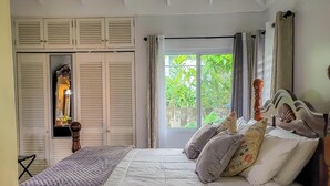 Een slaapkamer met een groot bed, een plafondventilator, een airconditioningapparaat, een raam met gordijnen en een kledingkast met verstelbare deuren.