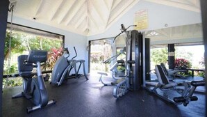 Een fitnessruimte met cardiotoestellen, gewichten en een groot raam met uitzicht op groen.