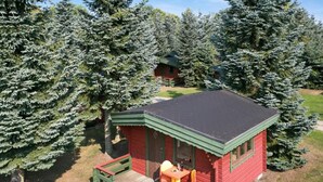 A small red cabin with a green porch and a table and chairs, surrounded by evergreen trees. - 4 Person Holiday Park Home in Graested (Graested)