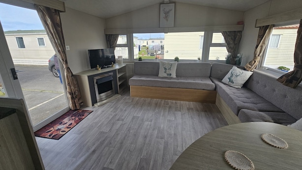 A compact living space with a sofa, a television, and a small entertainment unit. - Ruby a Modern Caravan in Rhyl (Rhyl)