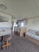A compact living space with a kitchenette, a dining area with a table and bench, and a sofa.