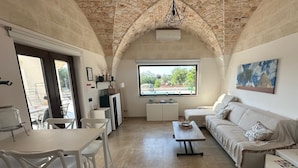 Ein geräumiger Wohnbereich mit hoher, gewölbter Decke, einem Esstisch mit Stühlen, einer Couch und einem Fenster mit Blick ins Freie.