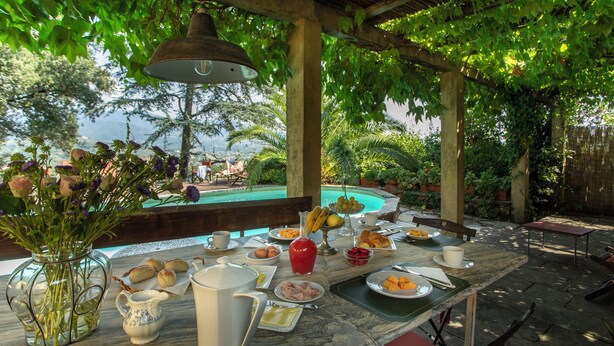 An outdoor dining area with a pool view, a table set with breakfast items, and a hanging light fixture. - VILLA PEDONE  (Lucca)