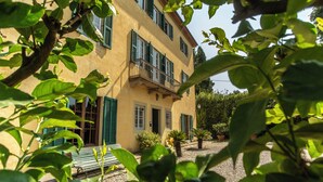 A two-story building with a balcony, surrounded by greenery and potted plants. - VILLA PEDONE  (Lucca)