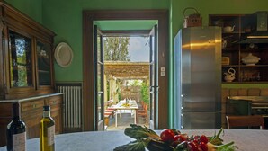 A kitchen with a marble countertop, a refrigerator, and a dining area visible through an open doorway. - VILLA PEDONE  (Lucca)