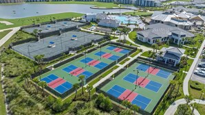 An aerial view of a residential area with multiple tennis courts, a swimming pool, and houses. - Gated area, Golfing, HOA Pool, Pickleball Courts, and Family Fun (Ave Maria)