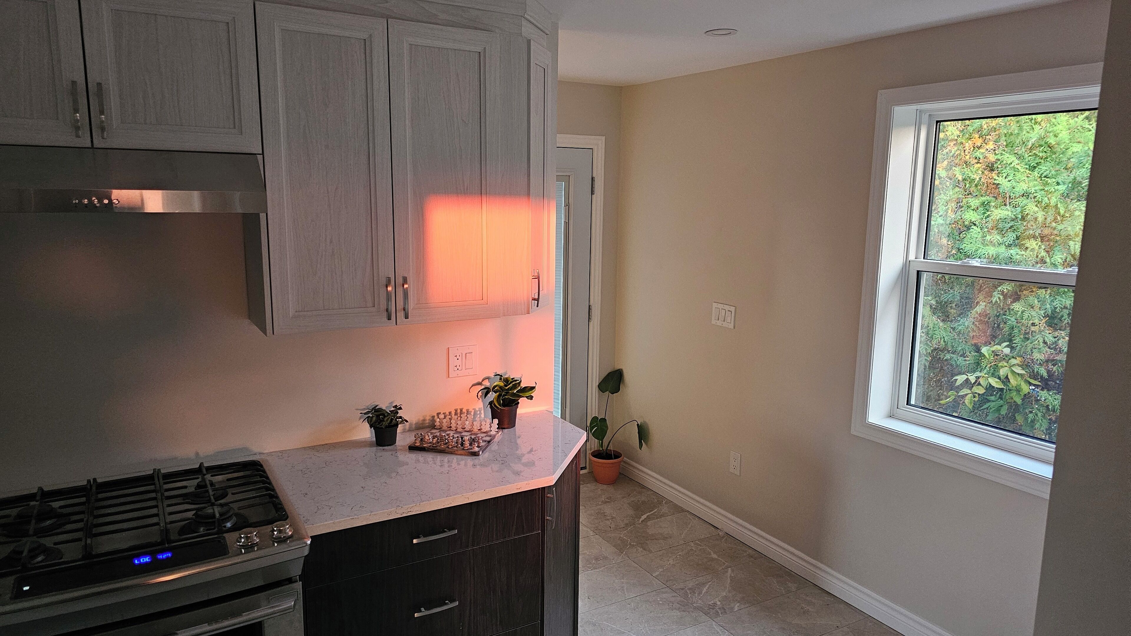A kitchen with grey cabinets, a stove, and a window with a view of trees.