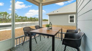 Een overdekt terras met een tafel, stoelen, een lantaarn en uitzicht op een huis en water.