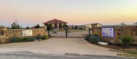 A gated entrance to a property with a stone wall, a metal gate, and a sign that reads "Bless on the River."