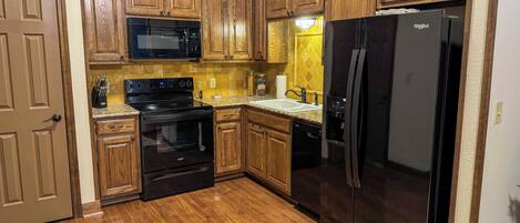 A kitchen with wooden cabinets, a black refrigerator, a microwave, a stove, and a dishwasher.