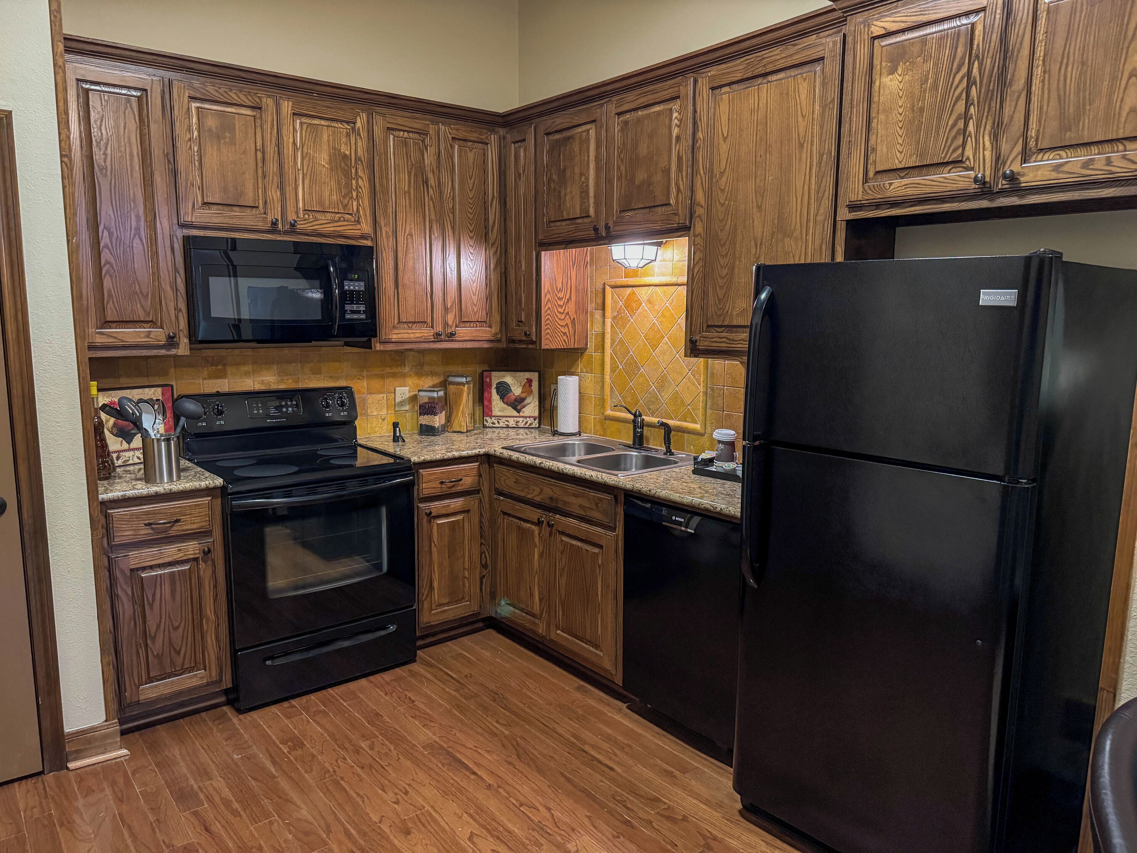 A kitchen with wooden cabinets, a black stove, a black refrigerator, and a microwave.