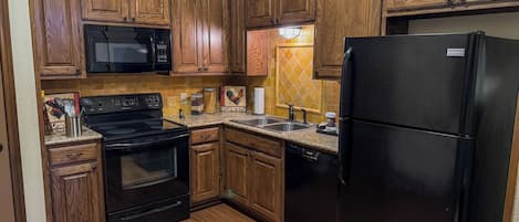 Une cuisine avec des meubles de rangement en bois, une cuisinière noire, un réfrigérateur noir et un four à micro-ondes.