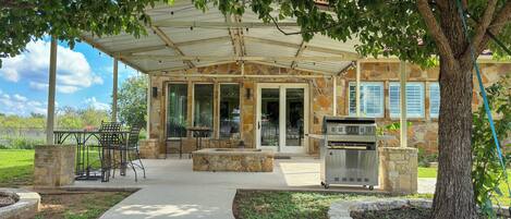 A covered patio area with outdoor seating, a grill, and a stone building in the background.