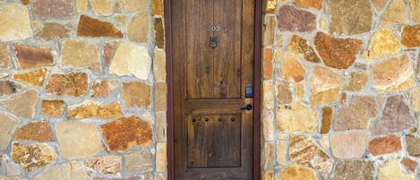 A stone wall with a wooden door marked "203" and a welcome mat.