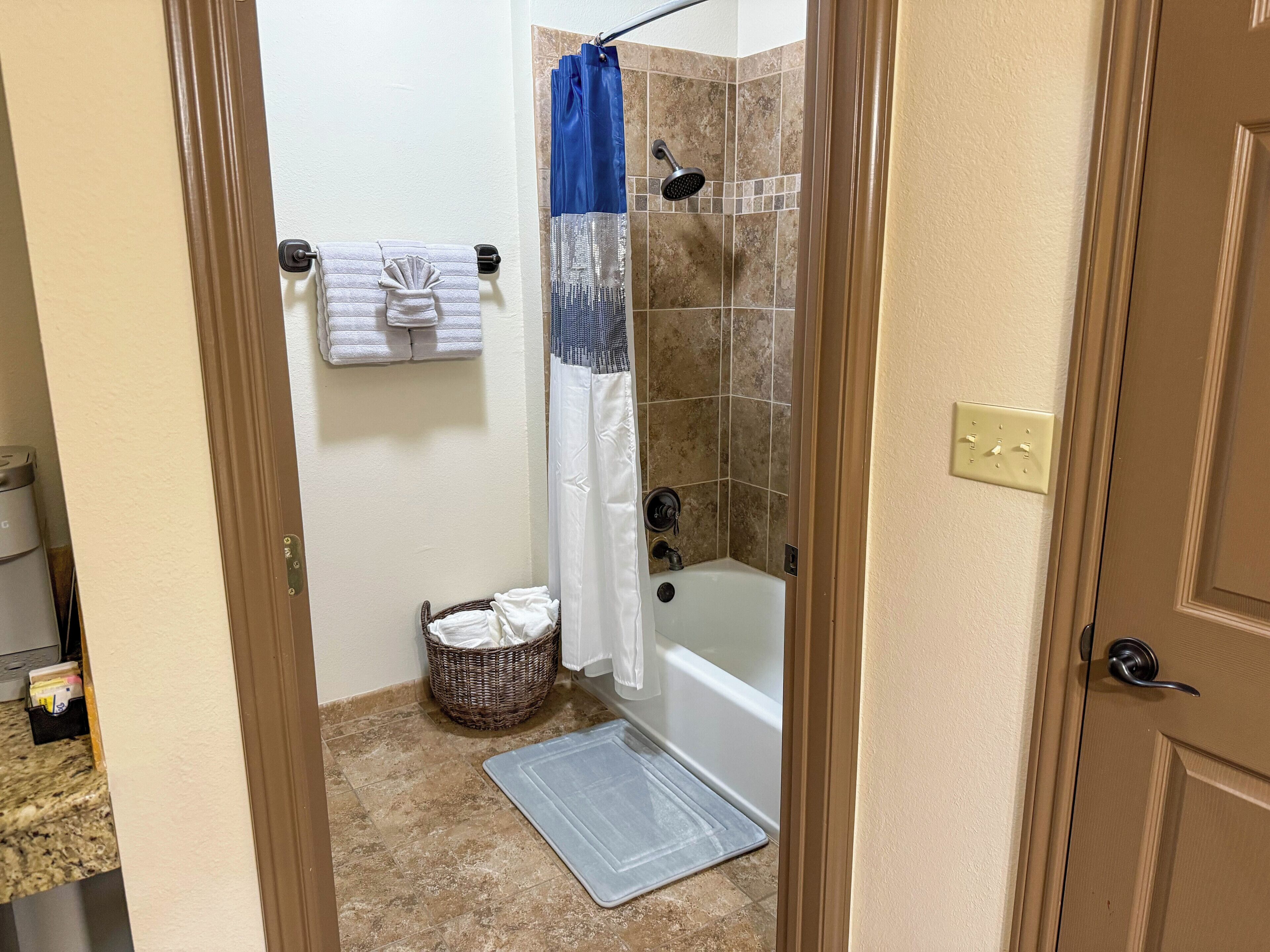 A bathroom with a shower, a bathtub, a towel rack with towels, a wicker basket, and a mat on the floor.