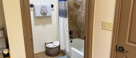 A bathroom with a shower, a bathtub, a towel rack with towels, a wicker basket, and a mat on the floor.