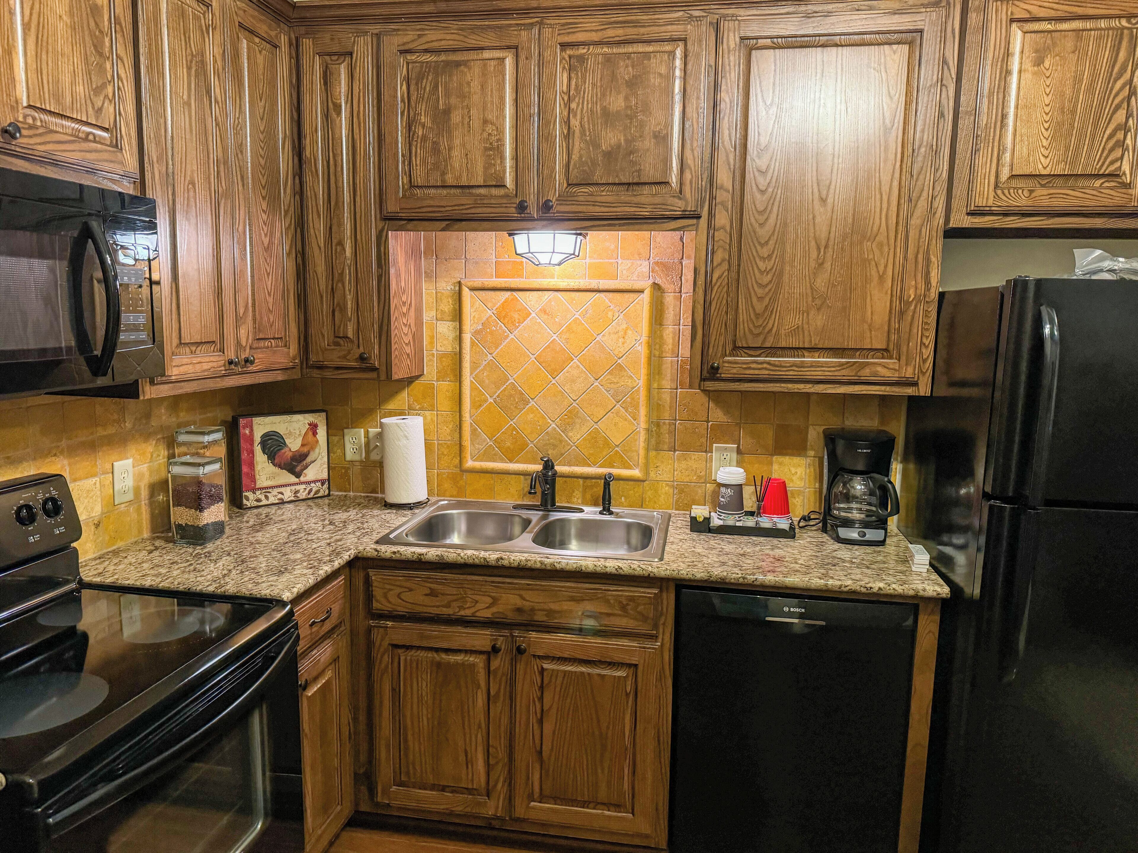 A kitchen with wooden cabinets, a stainless steel sink, a Bosch dishwasher, a black refrigerator, and a coffee maker.