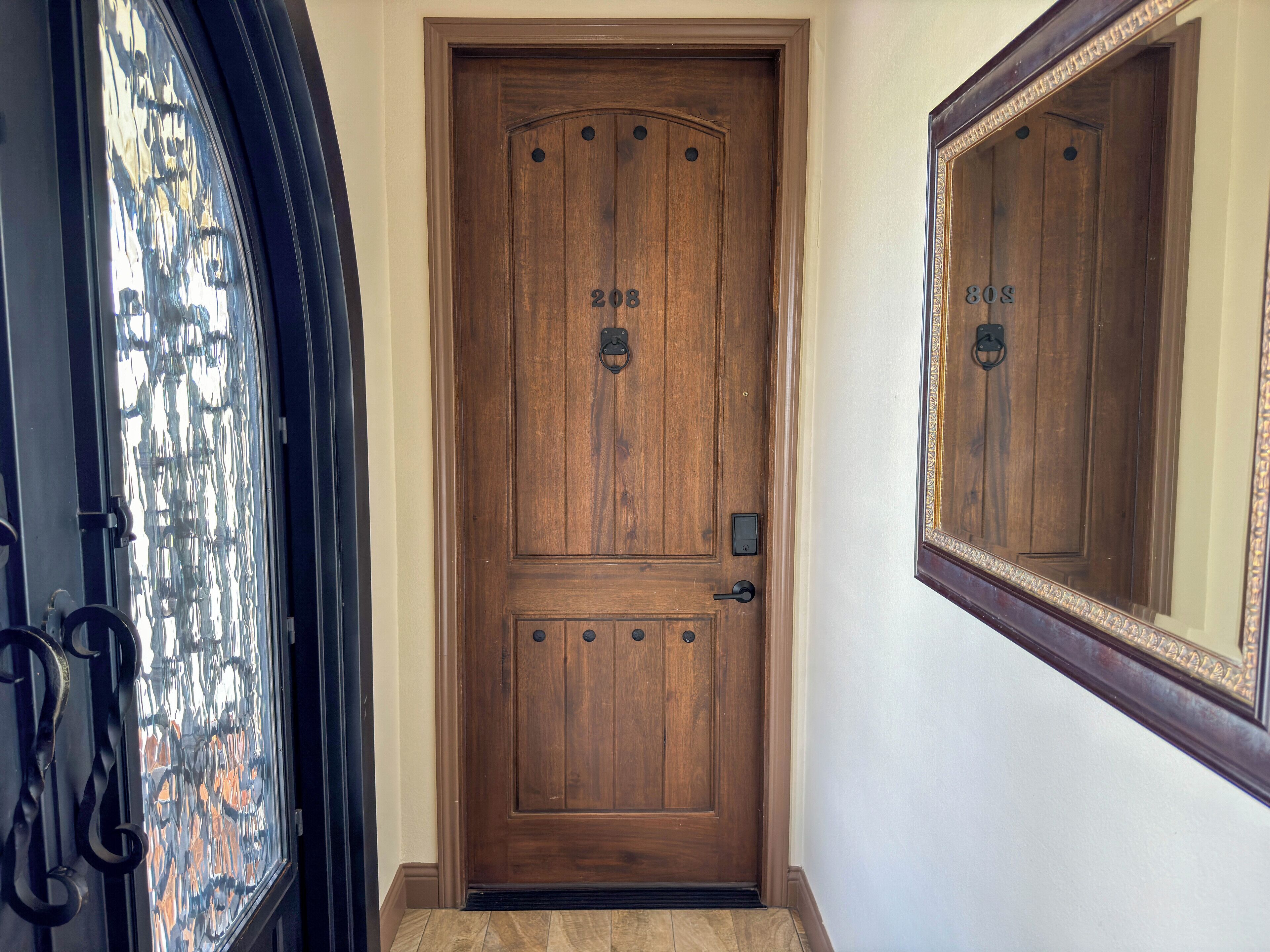 A wooden front door with a number plate, a small electronic lock, and a doorbell.