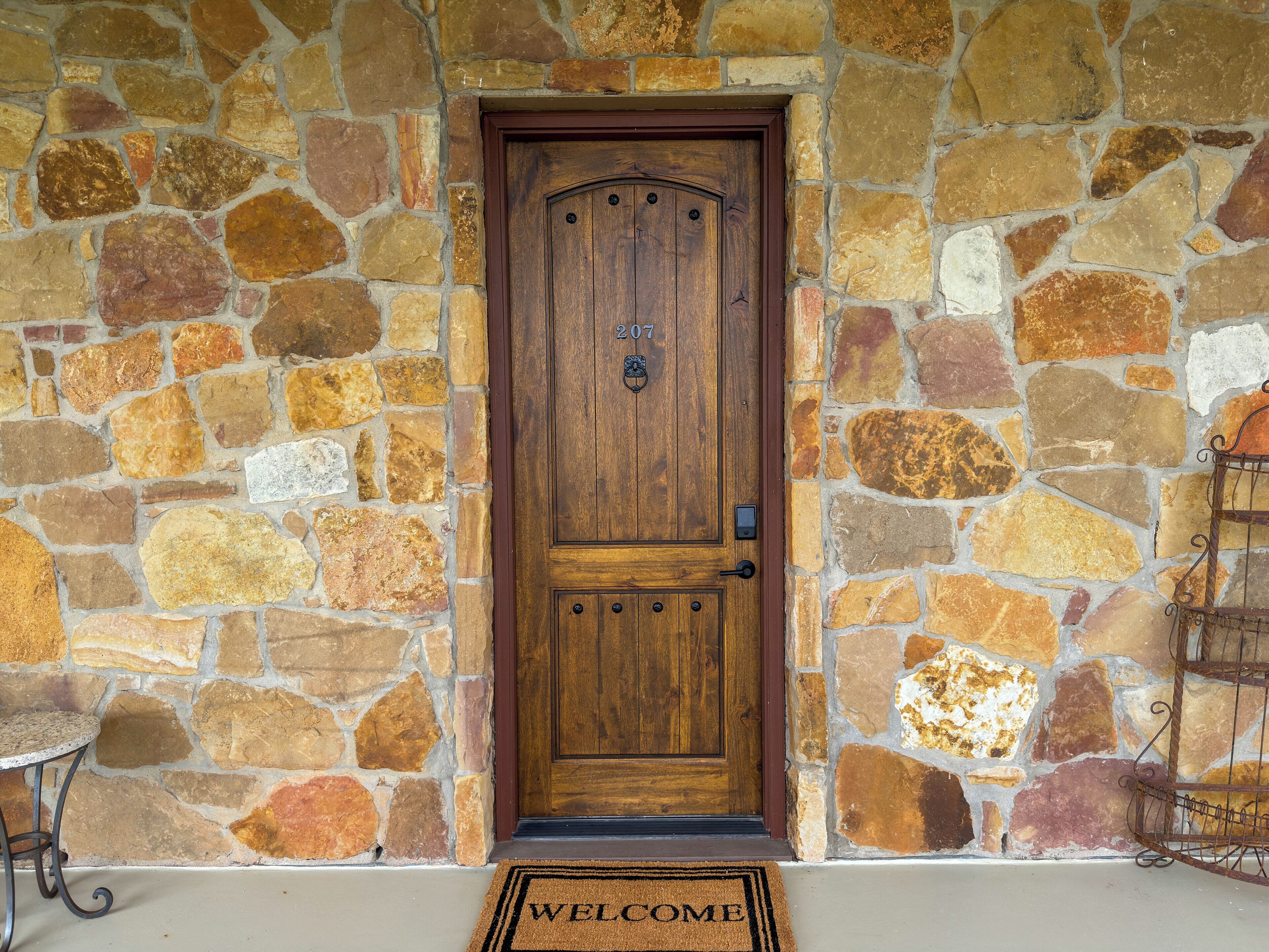 A stone wall with a wooden door, a metal doormat, and a metal rack.