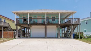 A two-story building with a balcony and a garage. - Mai Tide--4 BR House, Sleeps 11, Close to Beach, Dogs OK, Tons of Parking! (Port Aransas)