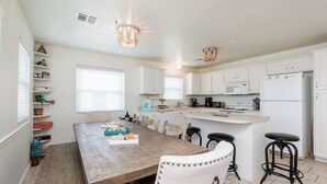A modern kitchen with white cabinets, a wooden dining table, and bar stools. - Mai Tide--4 BR House, Sleeps 11, Close to Beach, Dogs OK, Tons of Parking! (Port Aransas)