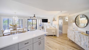 Una cocina amplia con una isla grande, una mesa de comedor de madera y sillas. Se observa un sofá blanco y un aparador decorativo con un espejo.